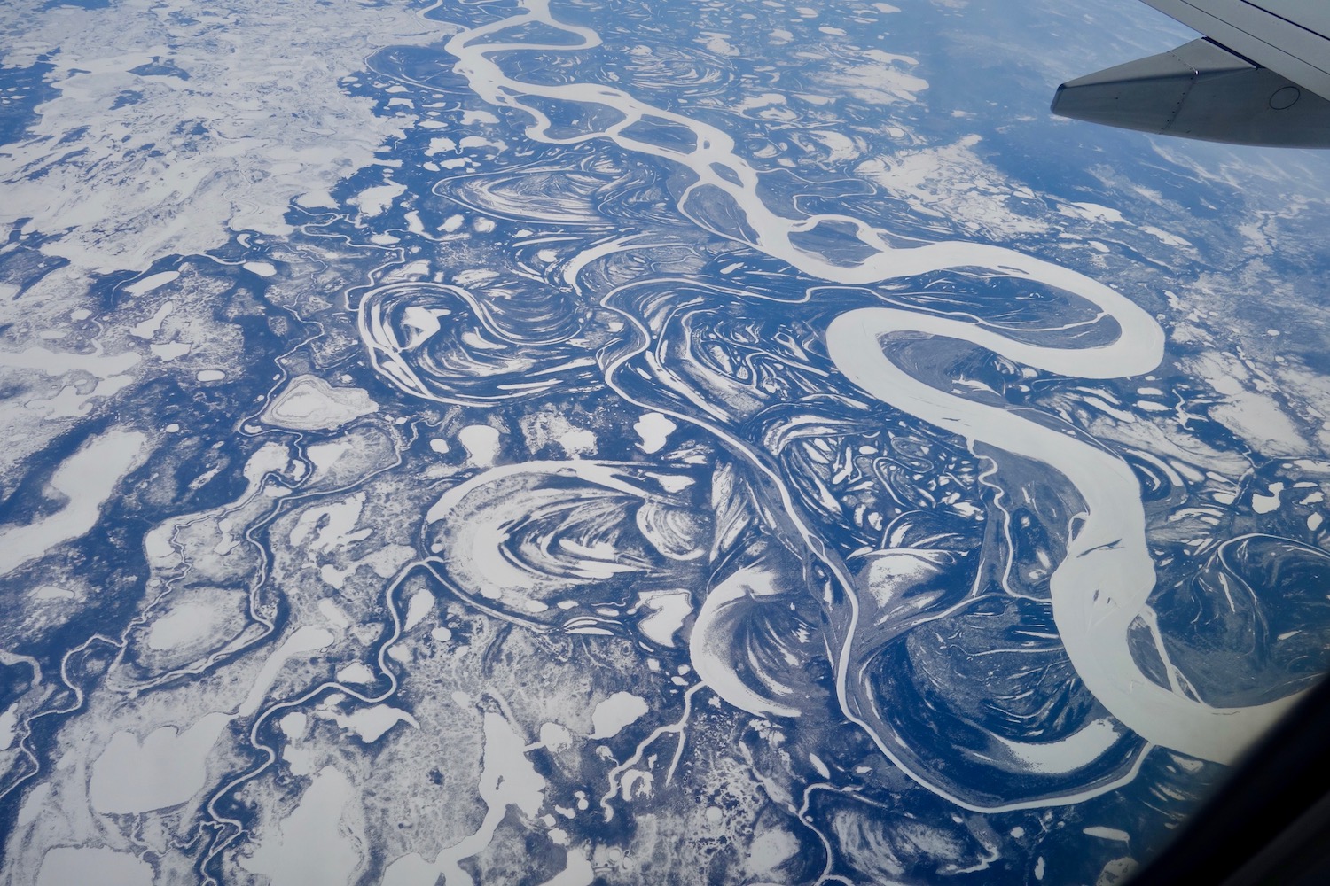 A large frozen river covered with snow meanders through a flatland sprinkled with oxbow lakes and smaller streams and rivers in this photo taken from a jet aircraft.