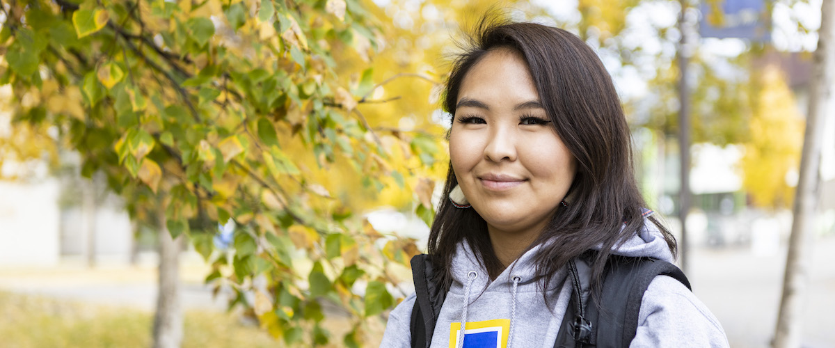Woman wearing University of Alaska sweatshirt and ulu earrings smiles for the camera