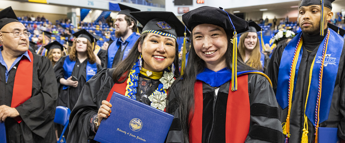 Two women wearing graduation regalia post for photo